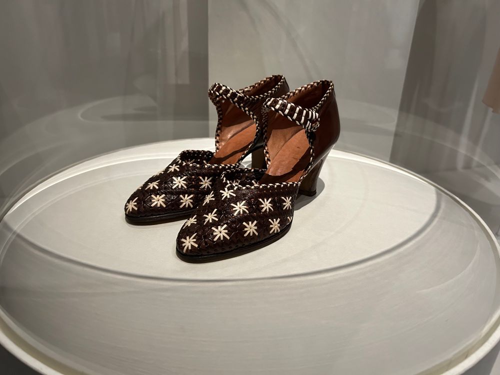 パンプス。ストラップ付きで、ヒールは高め。ブラウンの革に白い花のような模様が入っている。