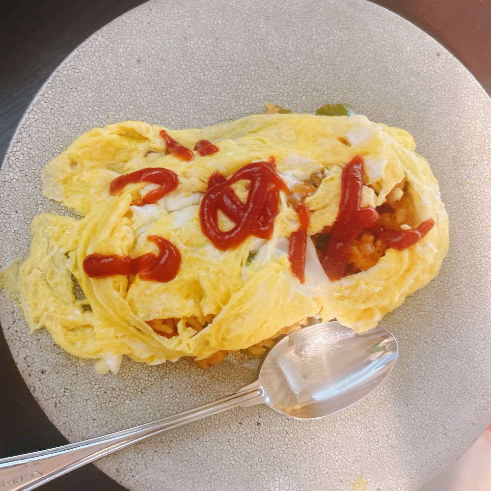皿に盛られたオムライスとスプーン。やや歪な卵の上にケチャップで「ごめん」と書かれている。