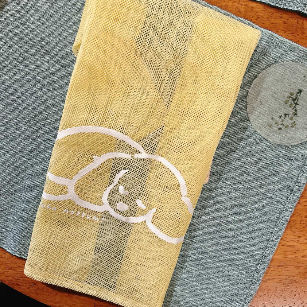 淡いイエローのメッシュバッグ。フロントにてらおかなつみさんイラストの白い犬のイラストがある。