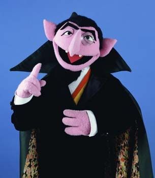 The Count from Sesame Street. He's a purple vampire with the traditional "Dracula Costume" for his outfit. He wears a monocle on his left eye, his cap is green with a colorful floral (this is a guess as the interior is a little hard to read).