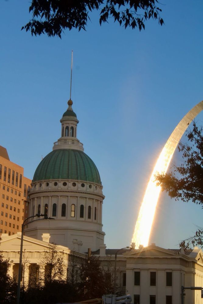 Sun glinting off the Gateway Arch with the Old Courthouse in the foreground. 