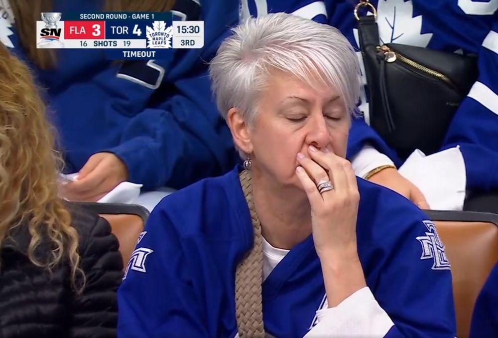 A Maple Leafs fan, an older woman with short silver hair with her eyes closed holding her mouth.