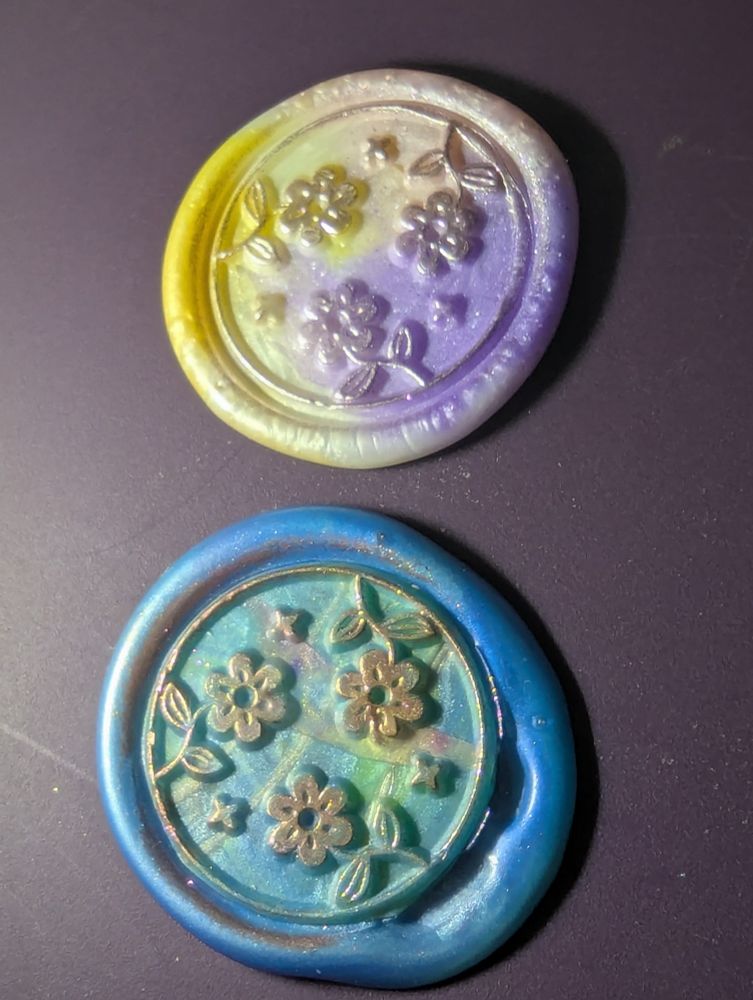 Two lighter tone wax seals with flower designs and holographic highlights