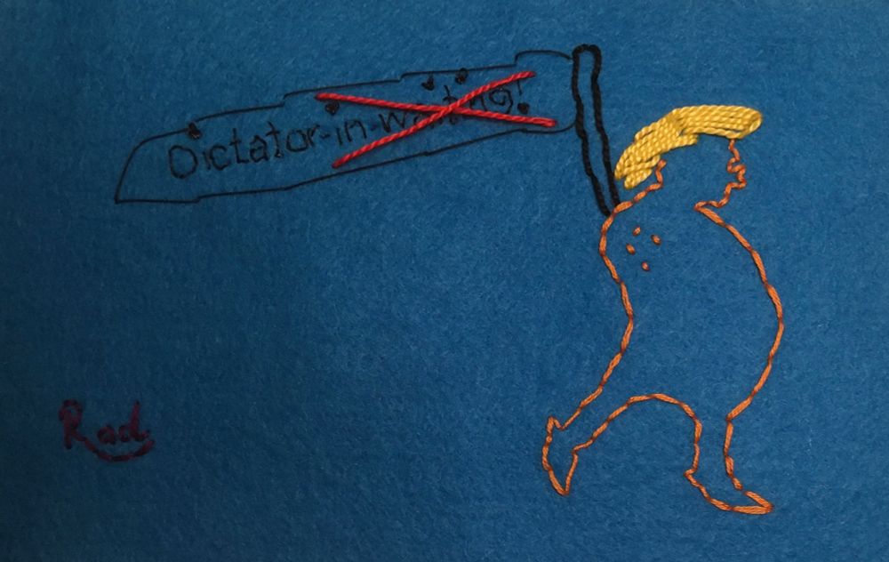 Embroidery of a Trump like version of ‘The Emperor with no Clothes’ carrying a banner with “Dictator-in-waiting” written on it. The “in waiting” part is now crossed out. 