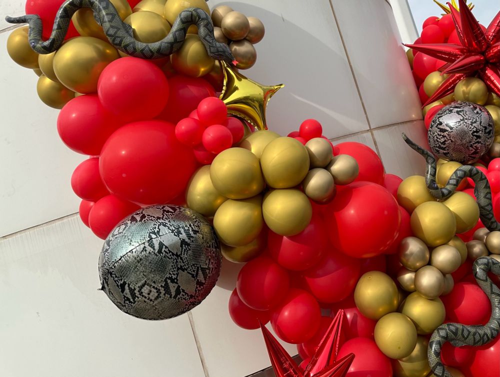 A photo of a display of red, gold, and snake balloons. The snake balloons are both circular with snakeskin pattern and balloons in the shape of snakes.