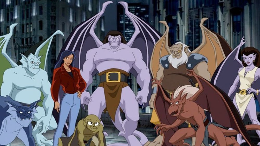 The cast of the animated series Gargoyles. Four more human looking gargoyles and three more animalistic ones and one human woman stand on a rooftop with skyscrapers behind them.