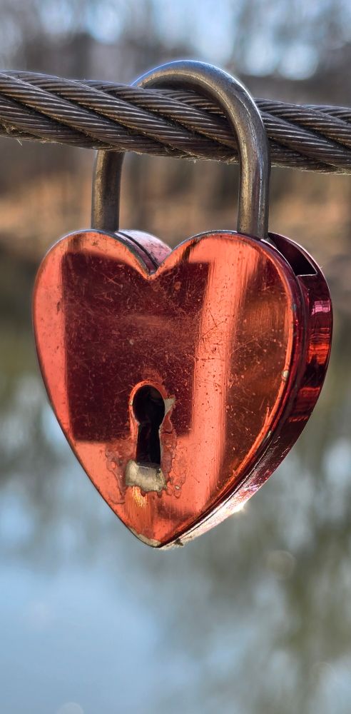 Ein rotes Schloss in Herzform hängt an einem Stahlseil. Man sieht ein Schlüsselloch.