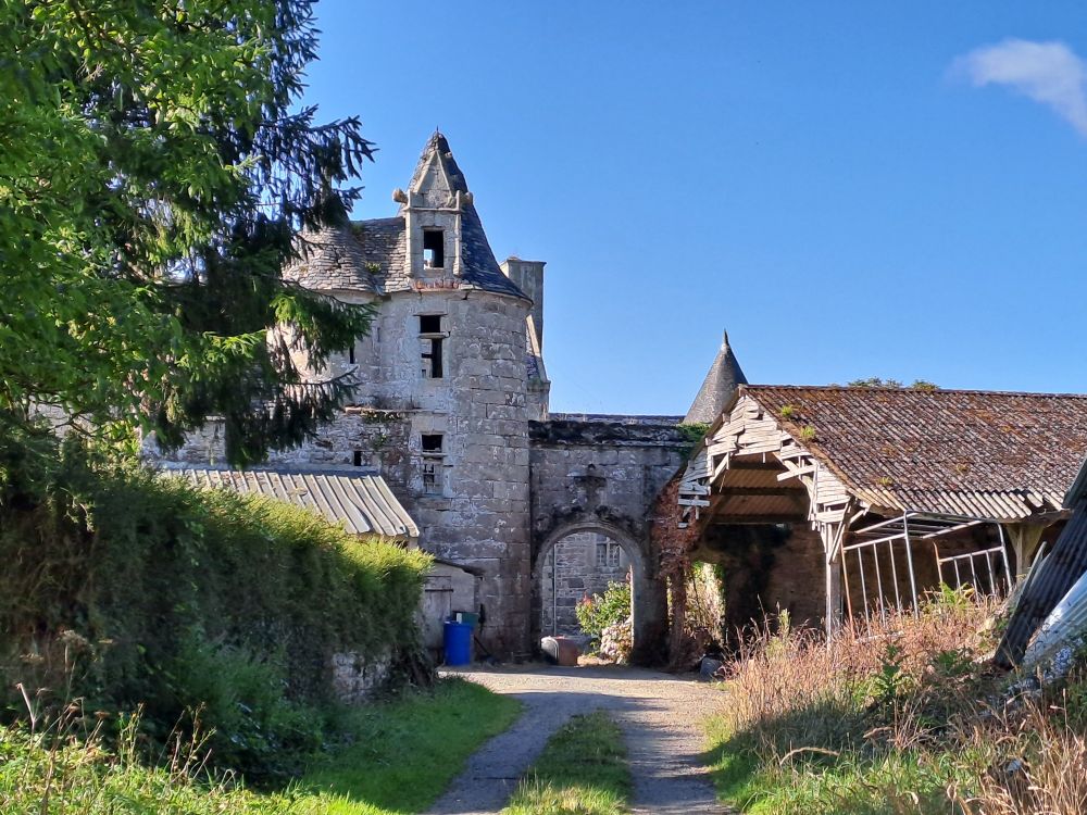 Entrée principale de Manoir de Tremerzit : grande porte cochère flanquée à gauche de deux tours à toiture conique. En avant du mur, de part et d'autre de la porte, deux hangars agricoles.