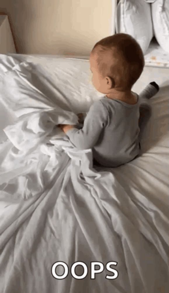 a baby is laying on a bed with a white blanket and the word oops is on the bottom of the picture