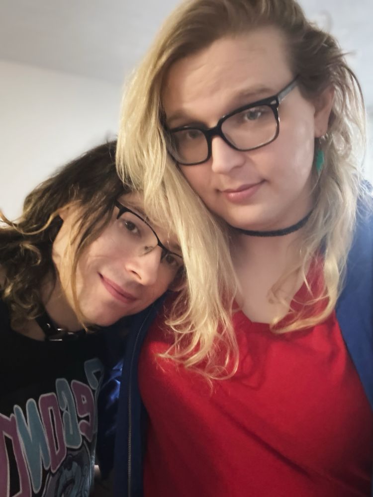 a selfie of my partner (brunette, wearing a collar) and i (tall blonde)