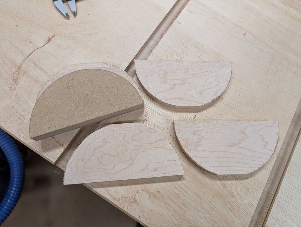 A half-circle template sitting atop four rough-cut pieces of maple wood, getting ready to be shaped to match the template.