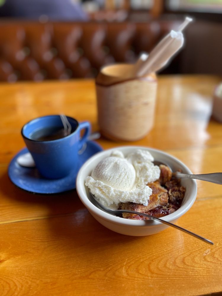 Rhubarb pie with vanilla ice cream on top. A blue tea cup with tea and a cup with straws. Sitting on a dinner table top 