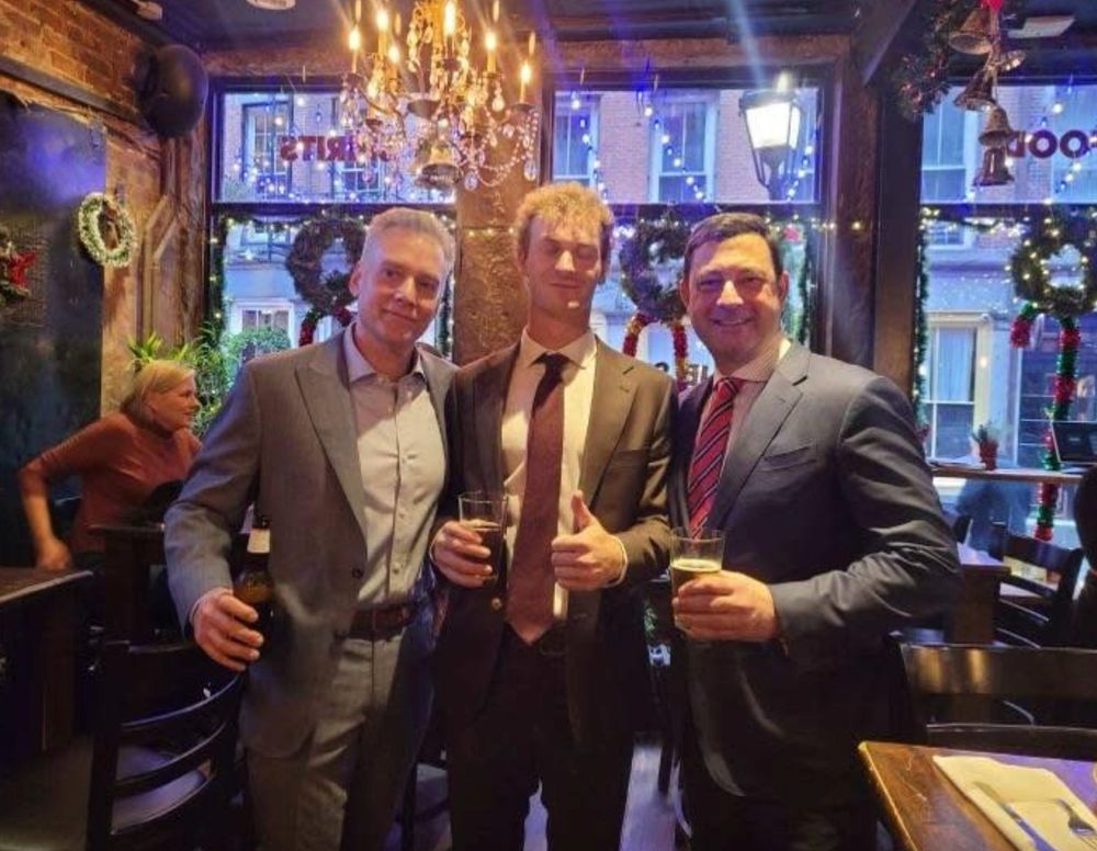 Daniel Perry and his lawyers at a bar holding drinks toasting to his acquittal. Perry is giving a thumbs up.