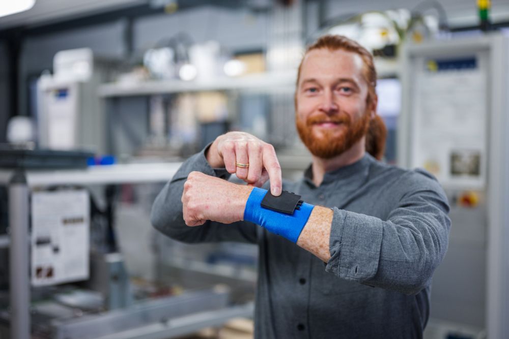 Wissenschaftler hält Arm hoch und zeigt auf ein Touchpad an einem Armband.