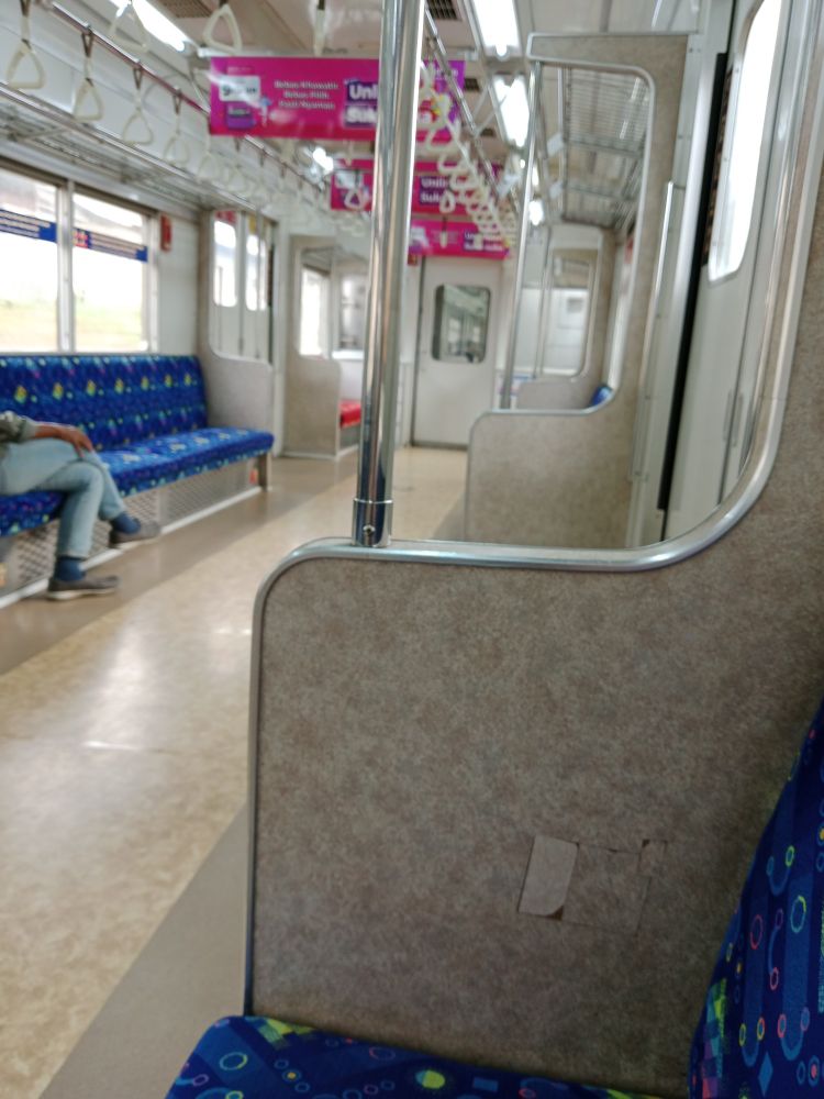 Picture of the empty half of a train coach with dark blue seats. On the left side of the picture is a pair of jeans-encased legs.