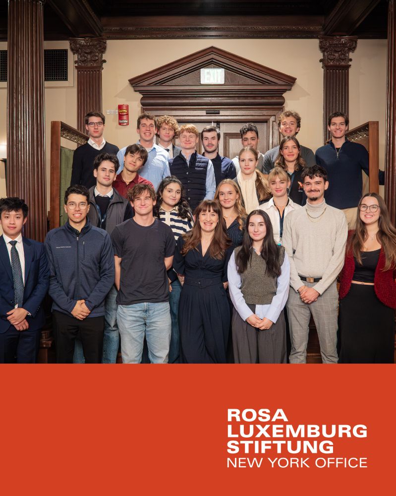 Heidi Reichinnek steht mit vielen studierenden vor einer alten Holztür, eingerahmt von Säulen aus Holz. Alle posieren für ein Gruppenfoto. Unten ist das Logo der Rosa-Luxemburg-Stiftung New York Office zu sehen.