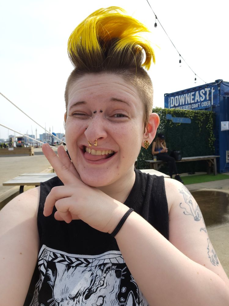 A photo of me. My hair is flipped in a way where it's standing up. I'm holding my hand under my chin, grinning with my tongue out. 