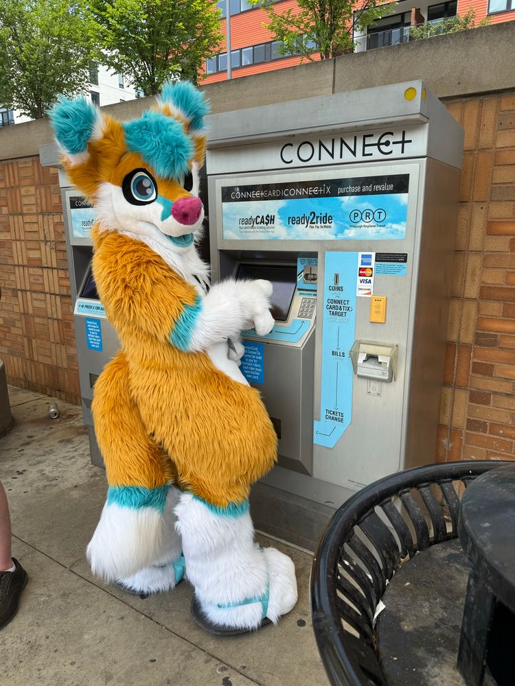 A fox fursuiter standing in front of a ticket machine