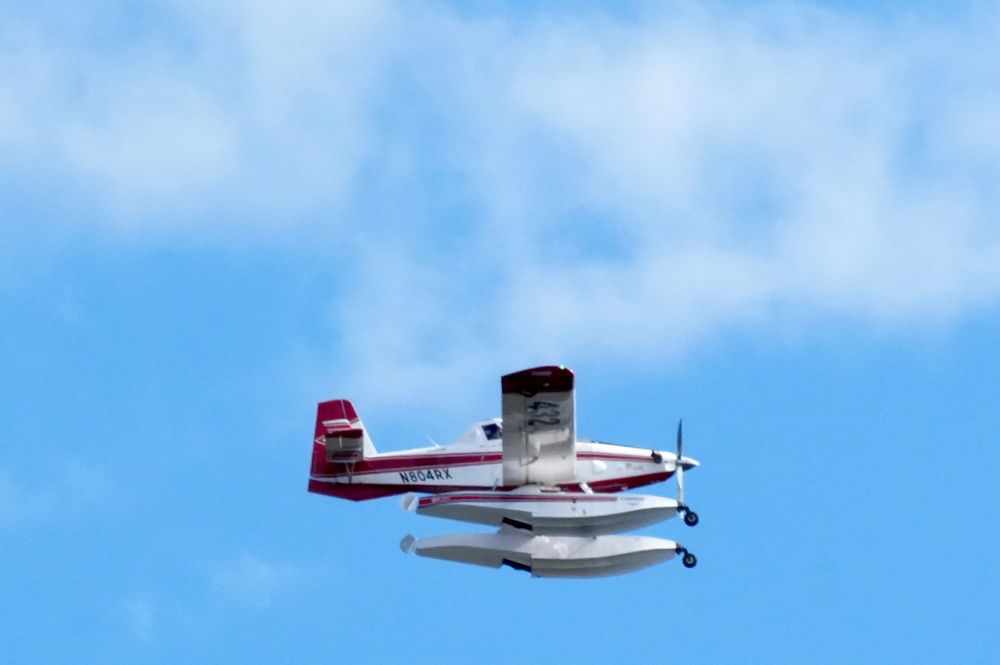 Photo of a Fire Boss air tanker headed toward a wildfire in Southeast Salem, Or on July 9. The plane is a single engine air tanker that scoops 800 gallons of water in 15 seconds. On this day we saw two of these planes heading toward the fire, then back toward the Willamette River to reload. After three or so passes, the fire was contained. The plane in the photo is white with red stripes. Blue sky and wispy clouds in the background.