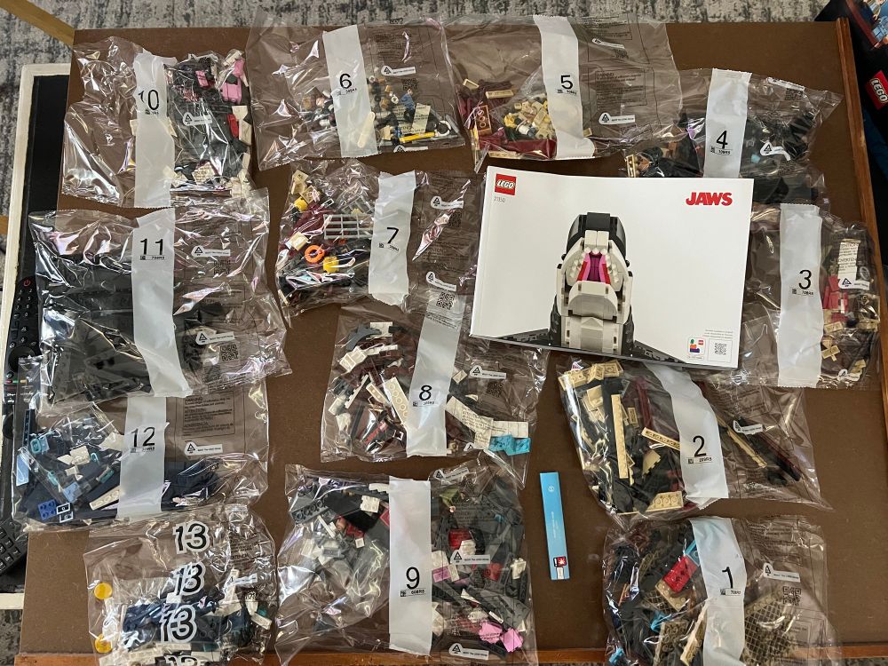 Photo of Jaws Lego set. Bags with Lego pieces, numbered 1-13, are laid out on a table with a 134 page instruction book 