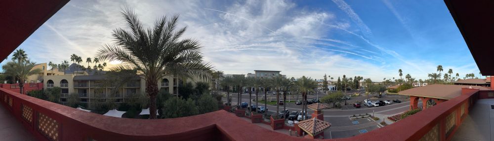 Panoramic view from a third floor roof deck of palm trees and buildings with mountains and desert in the distance