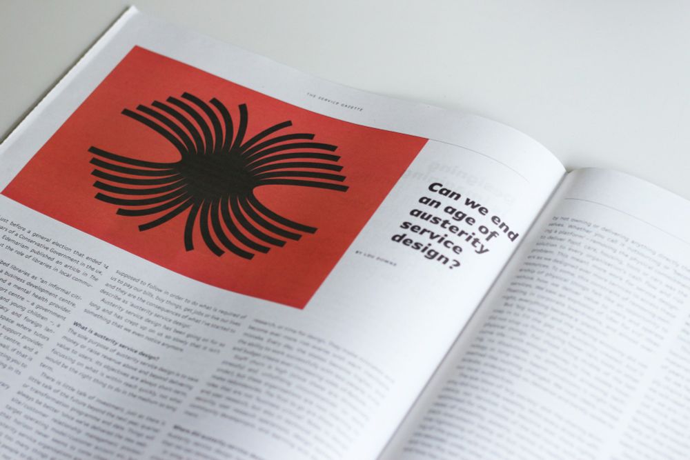 An open newspaper spread with 2 pages of text next to a big black and red graphic with the headline “Can we end an age of austerity service design?”