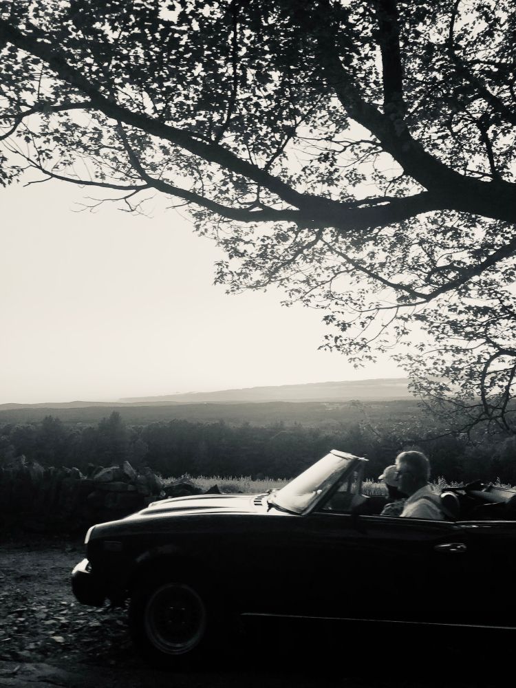 Black & white photo of a couple in a convertible at a scenic lookout 