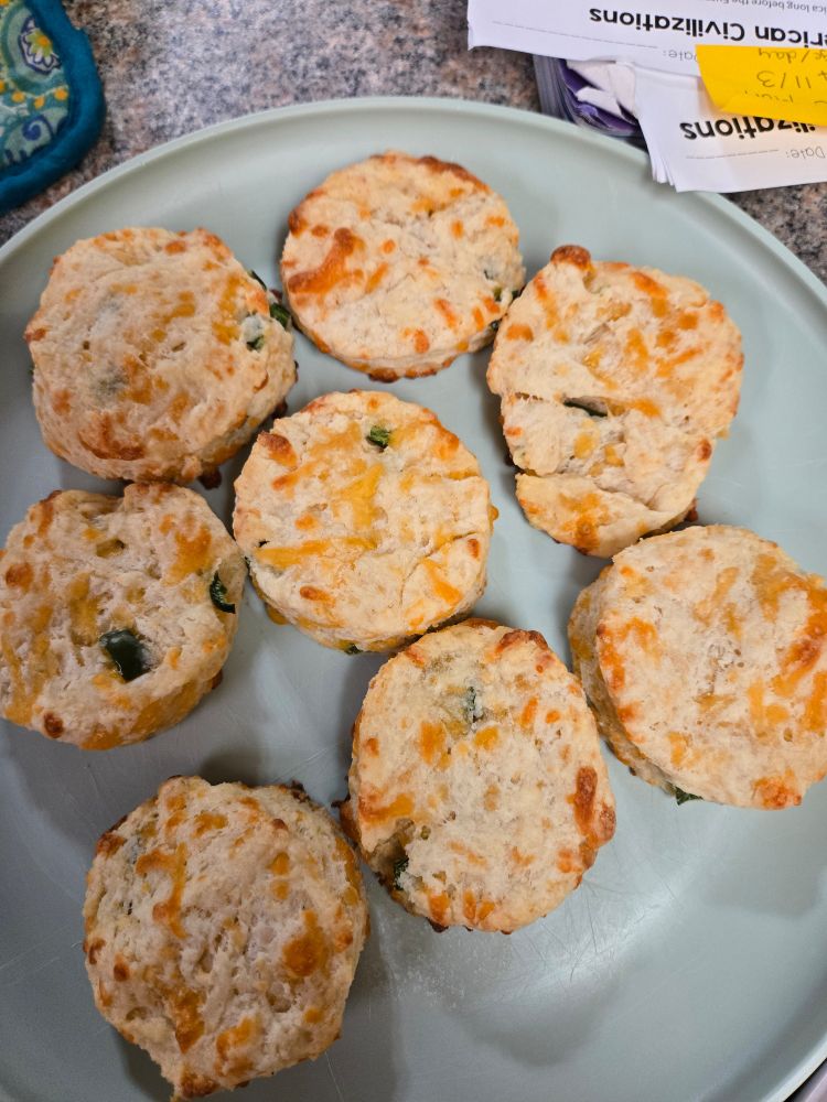 8 cheddar jalapeño biscuits on a green plastic plate with a bit of some homework nearby