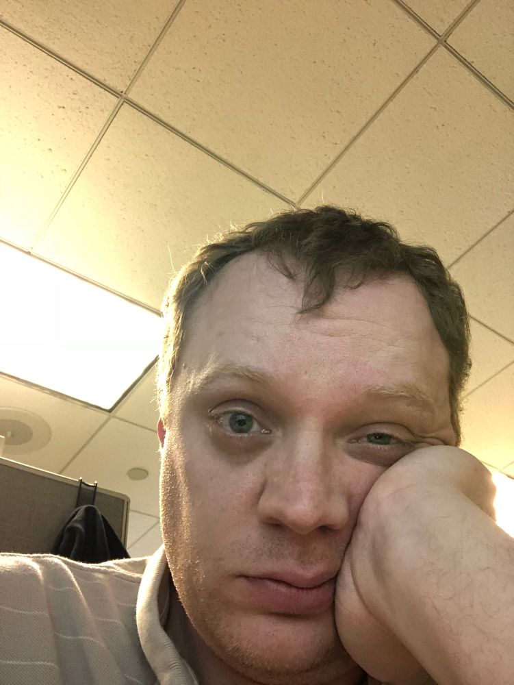 A very bored, frustrated, burned out me at my last social services job. I’m looking at the camera while leaning my head on my left hand. My hair is short and brownish-blonde. I have some stubble and I look extremely tired and kinda depressed.