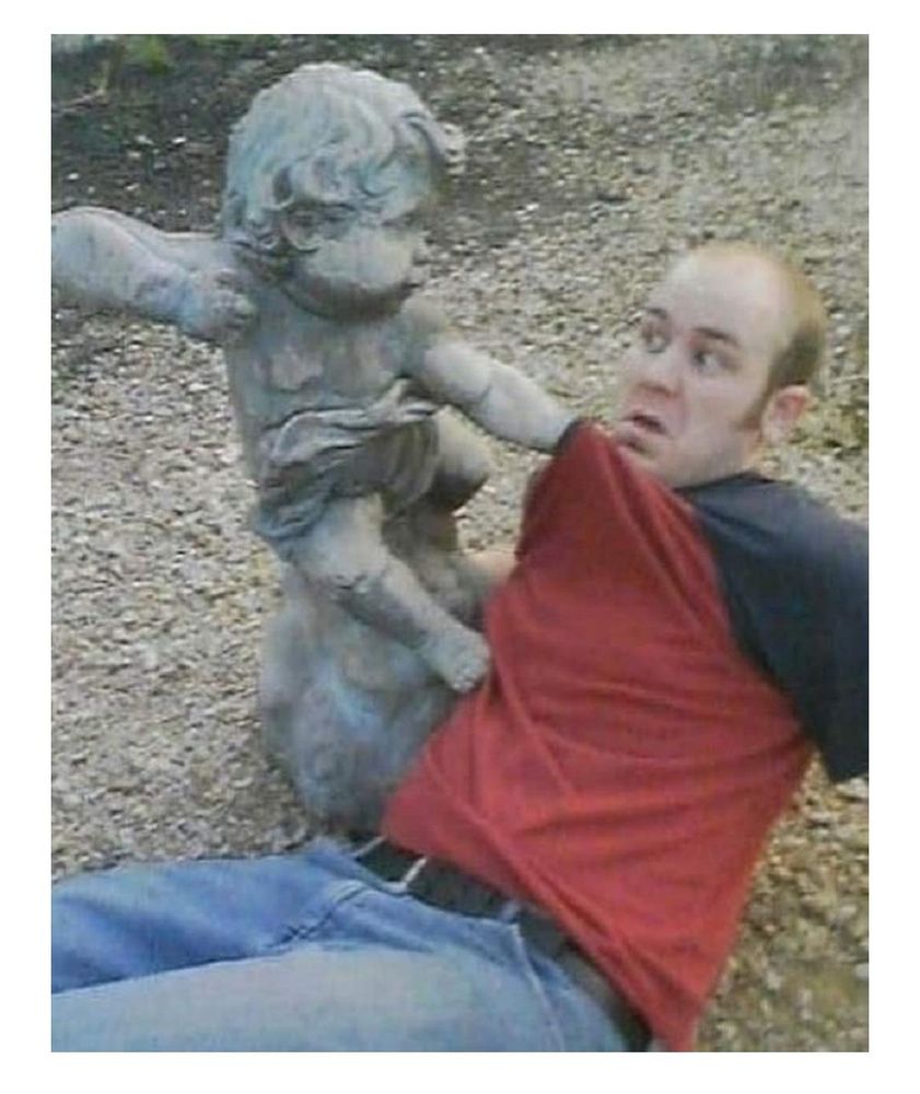 Une statue d'angelot qui lève un bras. Un homme s'est placé de telle sorte qu'on dirait que l'angelot le tape.