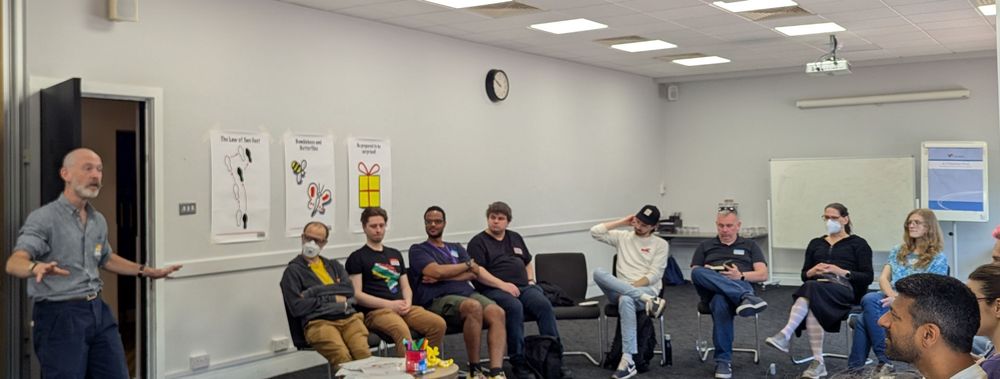 One person standing and a dozen people sitting in a circle. The posters in the background explain the open space principles.