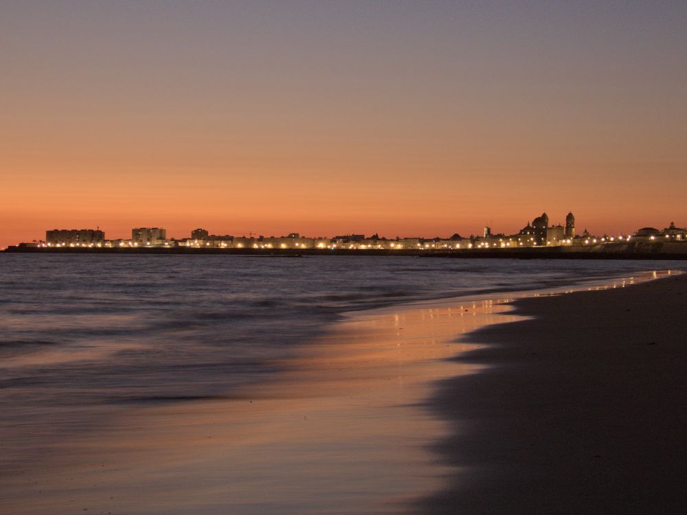 Vista del casco antiguo de Cádiz desde la playa Victoria durante el crepúsculo vespertino de ayer. Mar en calma poco antes de la entrada del cálido viento de Levante.