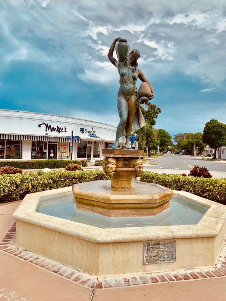 Bronze fountain statue of a woman holding two wine jugs- one on her shoulder the other at her side spilling into the fountain.  