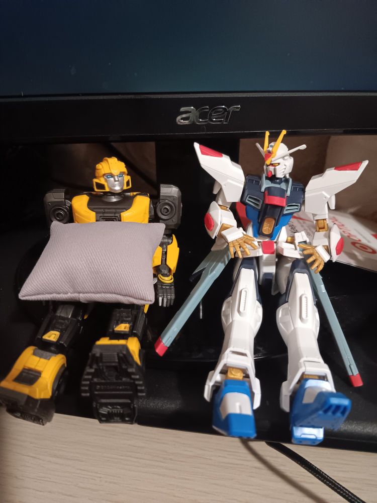 Yolopark cogless Bumblebee and HG Strike Freedom Gundam sit side by side underneath a monitor
