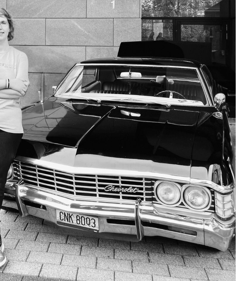 A picture of a 1967 Chevrolet Impala from the front. A woman is standing in front of it on the far left of the picture 