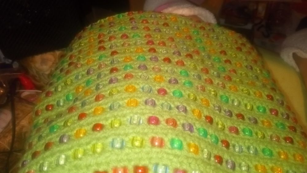 crocheted beaded blanket in progress the yarn used is green and the beads are multicolored 