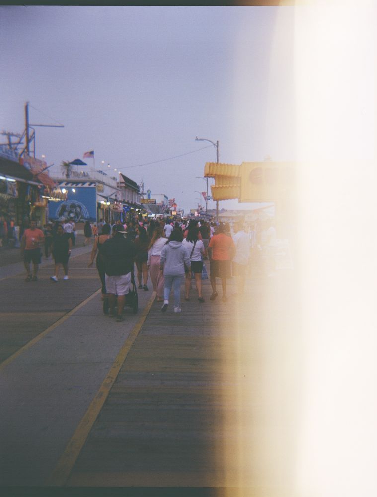 Film photo of a family walking toward a fry-stand on the boardwalk with a light leak on the right side of the photo