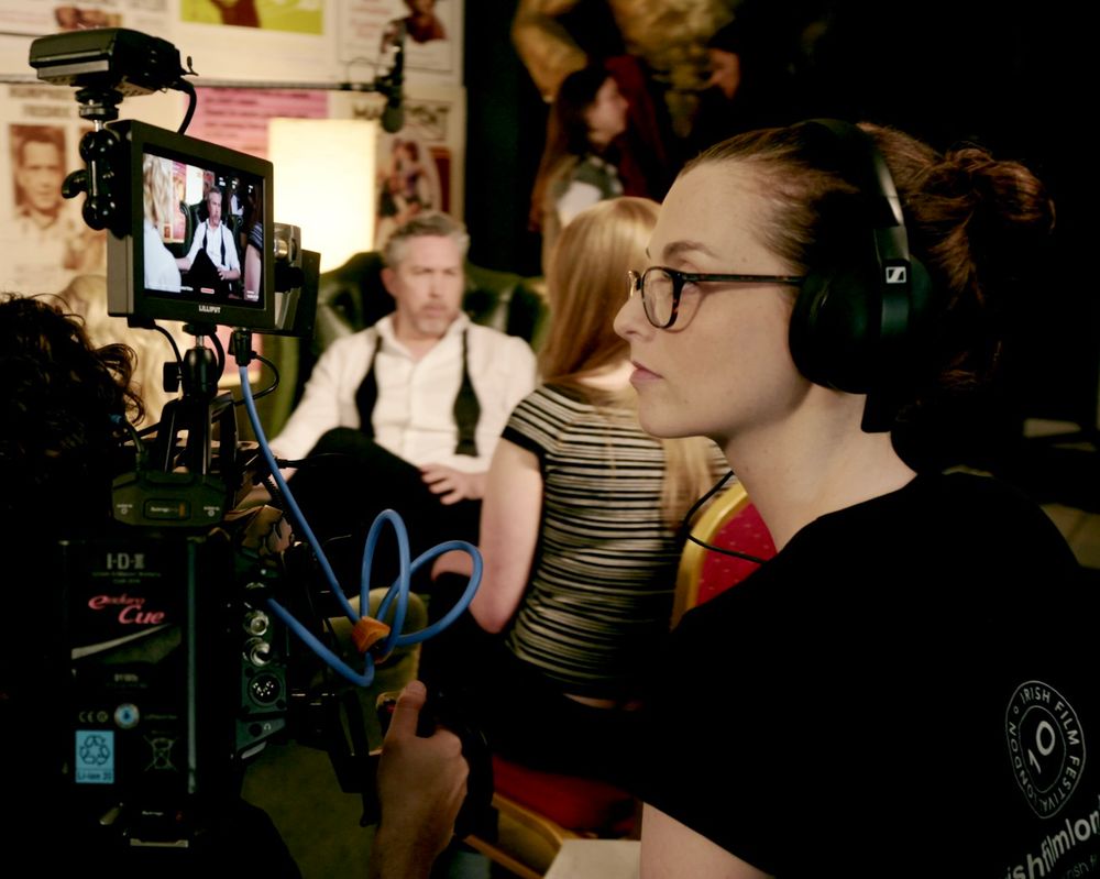 A picture of me wearing headphones and watching a monitor that’s mounted to a camera while actors are performing in the background. 