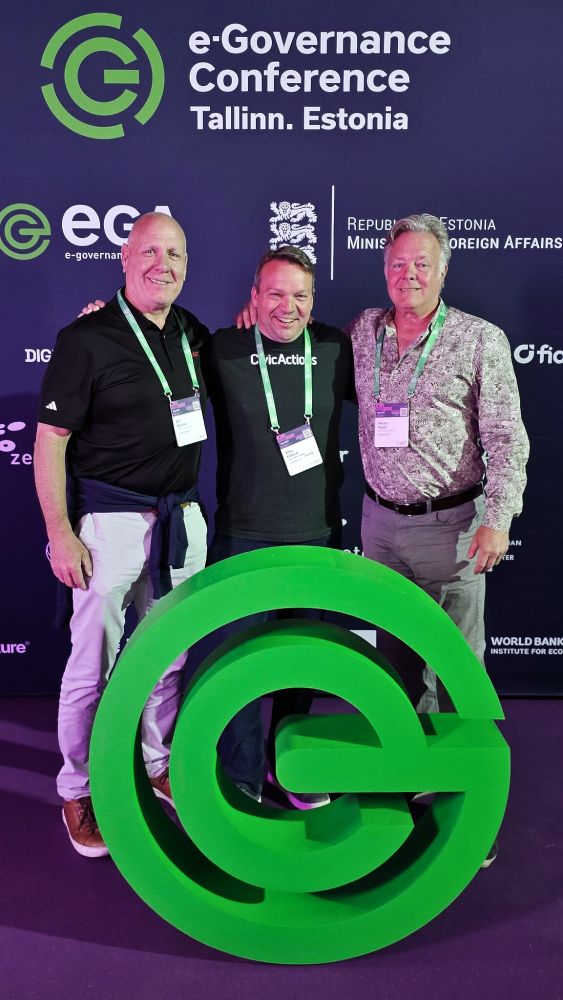 Mike Gifford, Henry Poole, and Bill Ogilvie pose in front of step and repeat at eGov2025 conference in Estonia