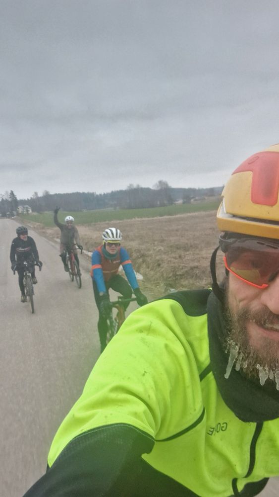 Selfie pyörän selässä. Taustalla kolme pyöräilijää ja heidän takana vihreä pelto.