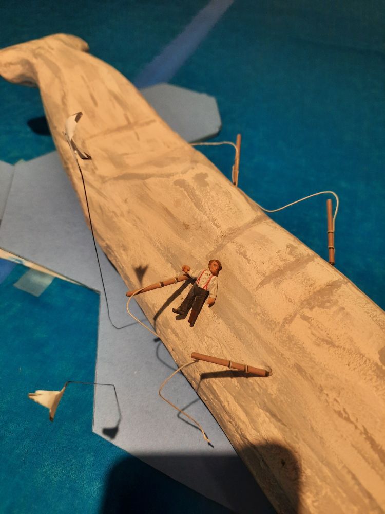 Close-up of a tabletop strategy game showing Moby Dick, bristling with harpoons, and with a tiny human figure stuck to his side.