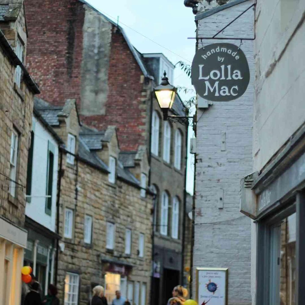 The hanging sign above the LollaMac shop, with the buildings of the street church away behind.