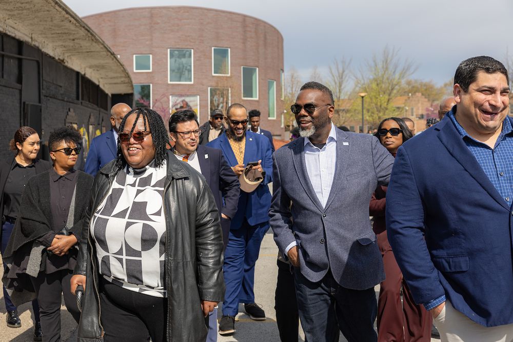 Mayor Brandon Johnson, First Lady Stacie Johnson, People for Community Recovery Executive Director Cheryl Johnson, Alderman Peter Chico, Alderman Byron Sigcho-Lopez, and several other people walking together outdoors on a sunny day in Altgeld Gardens.
