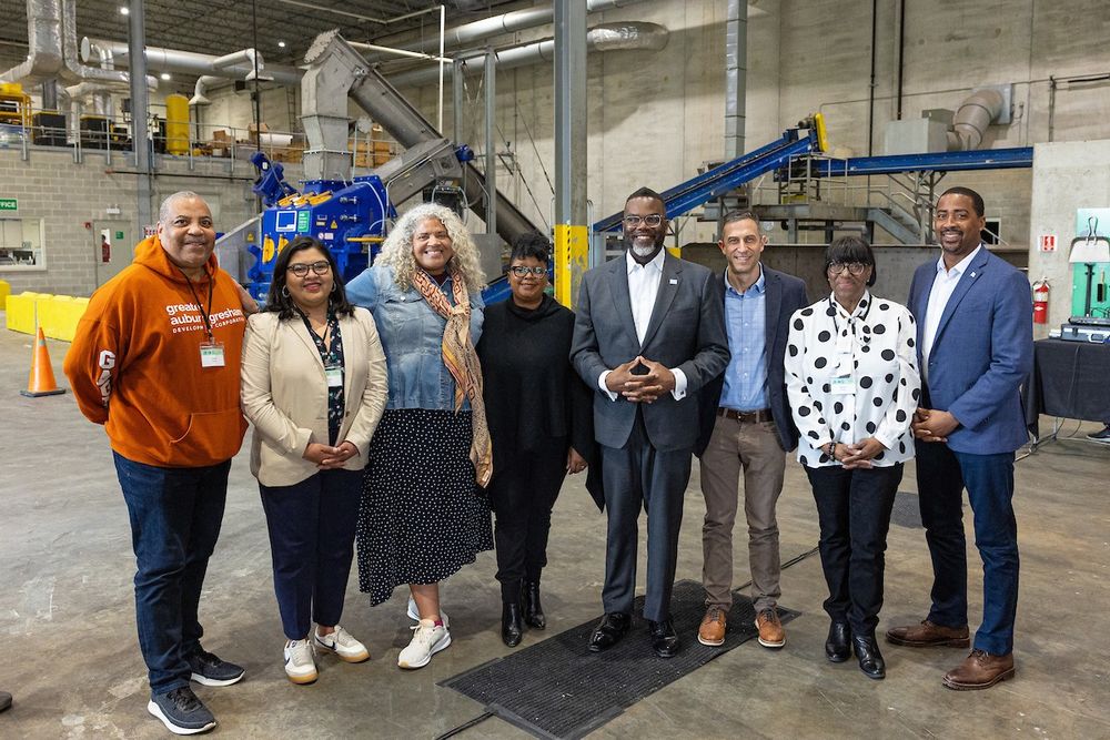Group of eight individuals posing together in an industrial setting, in front of Green Era's anaerobic digester, smiling at the camera.
