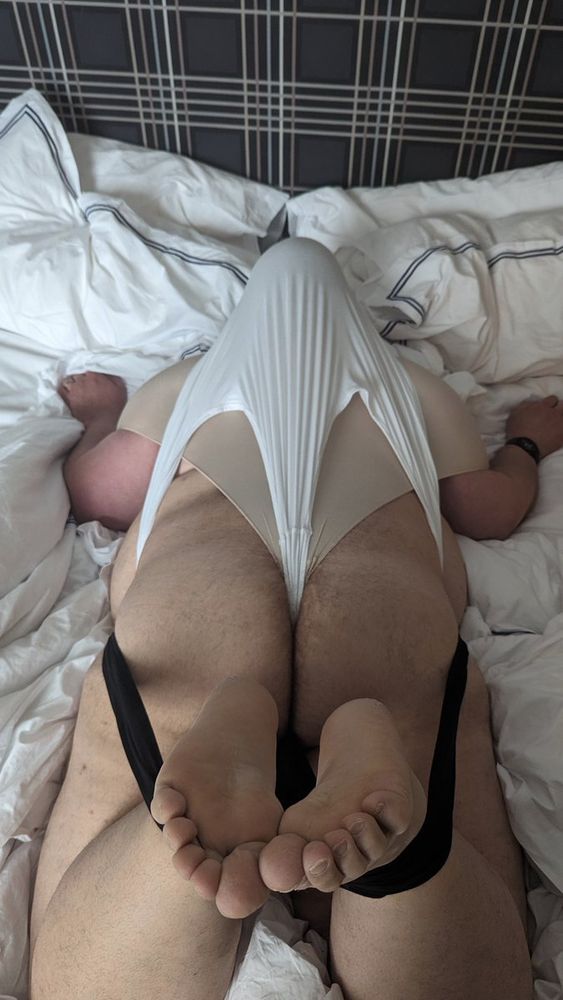 Rear view of me lying on my stomach on a bed wearing nothing but 3 pairs of underwear: a pair of black briefs that have been secured in a jock lock, a pair of tan panties that have been secured in a shoulder wedgie, and a pair of tighty whities that have been secured in an atomic wedgie