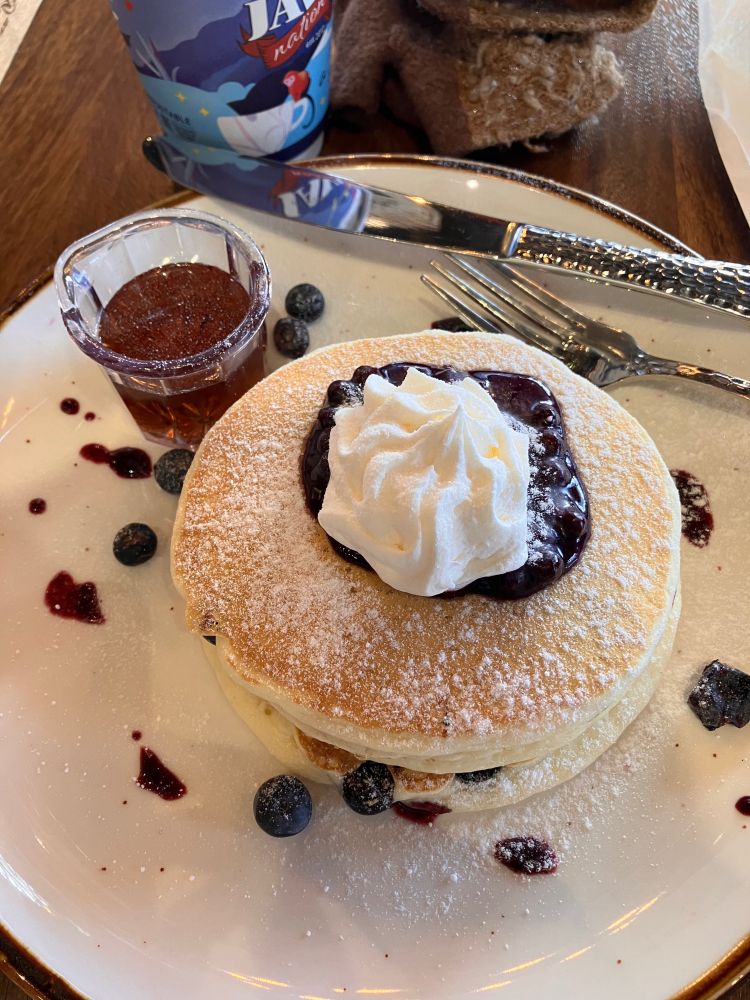 A photo of a stack of fluffy pale pancakes, topped with berry compote and whipped cream, and dusted with a light coat of powdered sugar