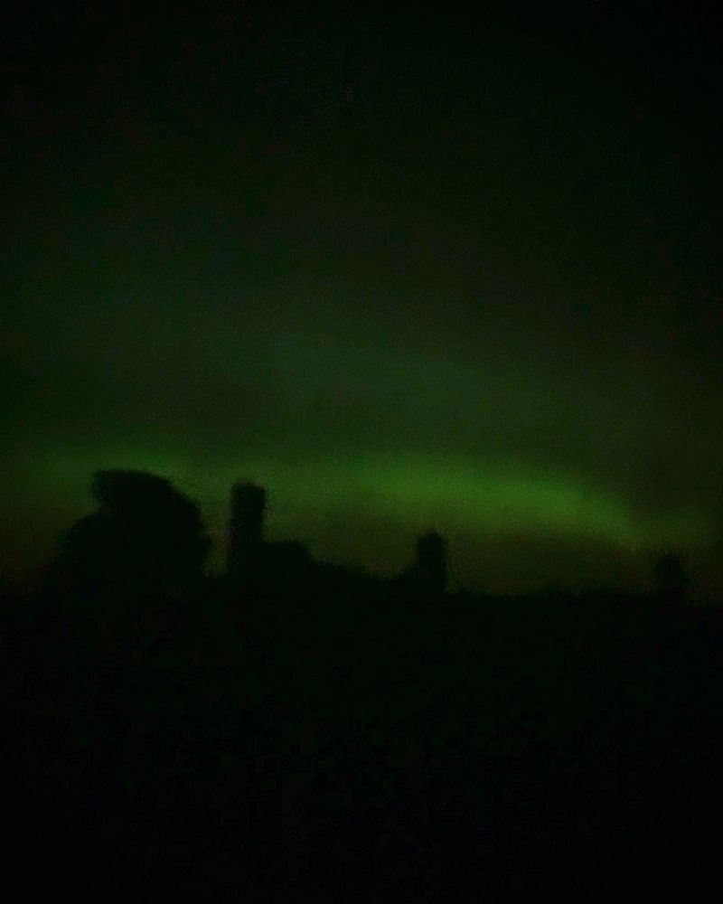 The northern lights with a blurry silhouette of farm buildings in the foreground.