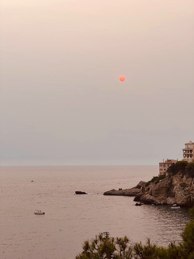 Atardecer.
El cielo y el mar están rojos. A la derecha hay unos barrancos con unas casas que cuelgan encima del mar