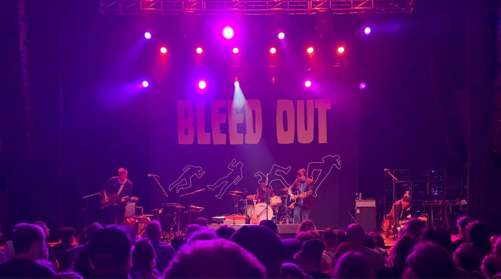John Darnielle and Co, with a Bleed Out banner at the back of the stage