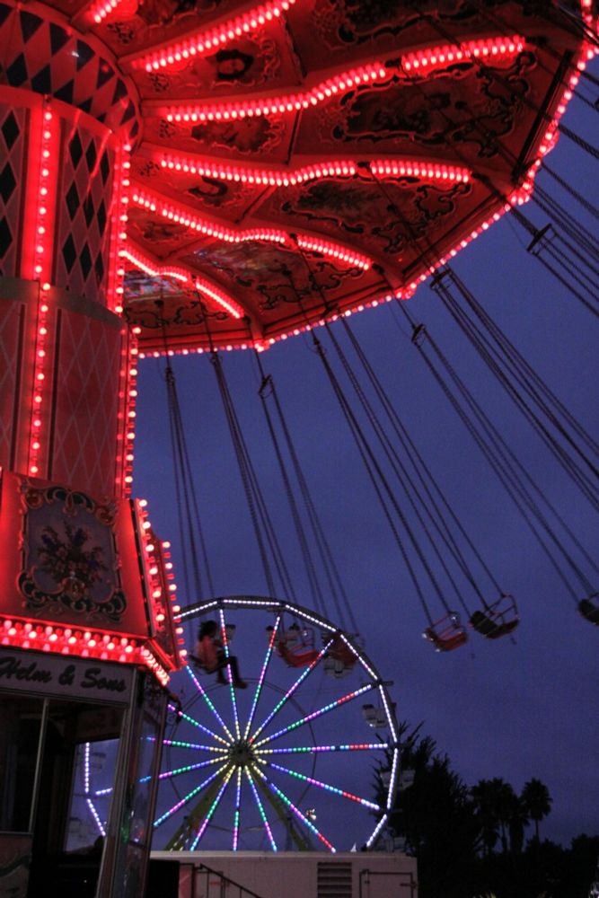 Fair rides lit up at night with the swing ride in the foreground and the ferris wheel in the background.